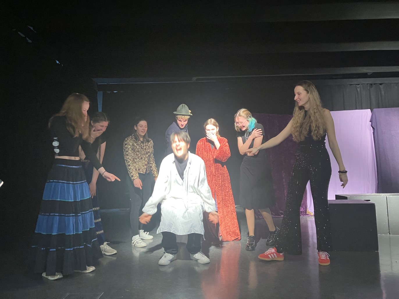 Acht Schülerinnen und Schüler spielen auf der Bühne Theater. Im Zentrum steht ein Junge mit weißem Kittel.