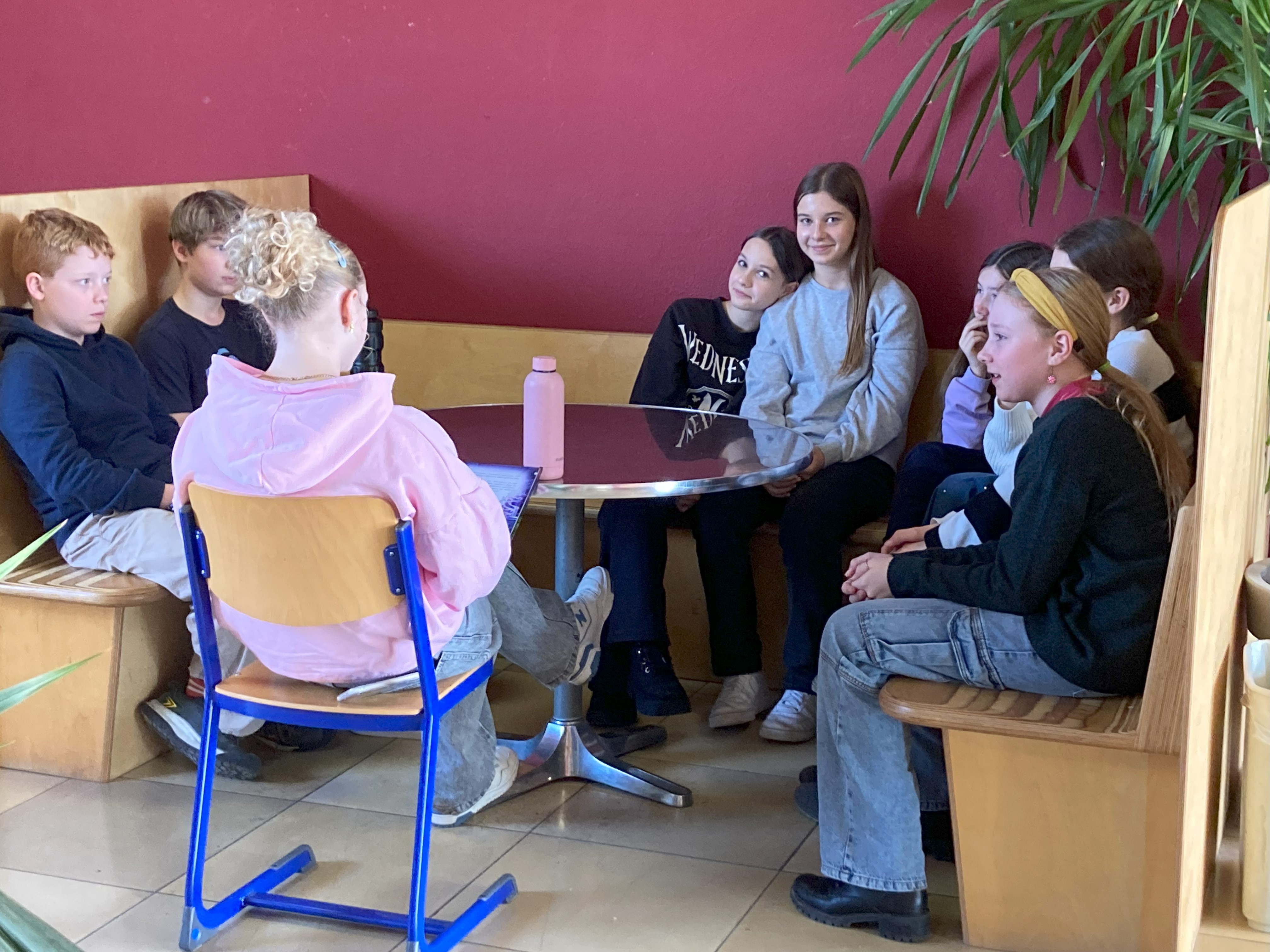 Schülerinnen und Schüler sitzen in einer Sitzecke des Gymnasiums. Eine ältere Schülerin liest vor.